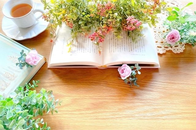テーブルの上に広げられた本の上に置かれた花束と紅茶